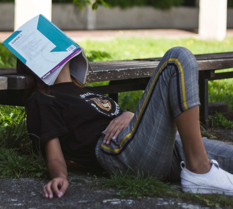 Girl sleeping on a park bench with her notebook on her face